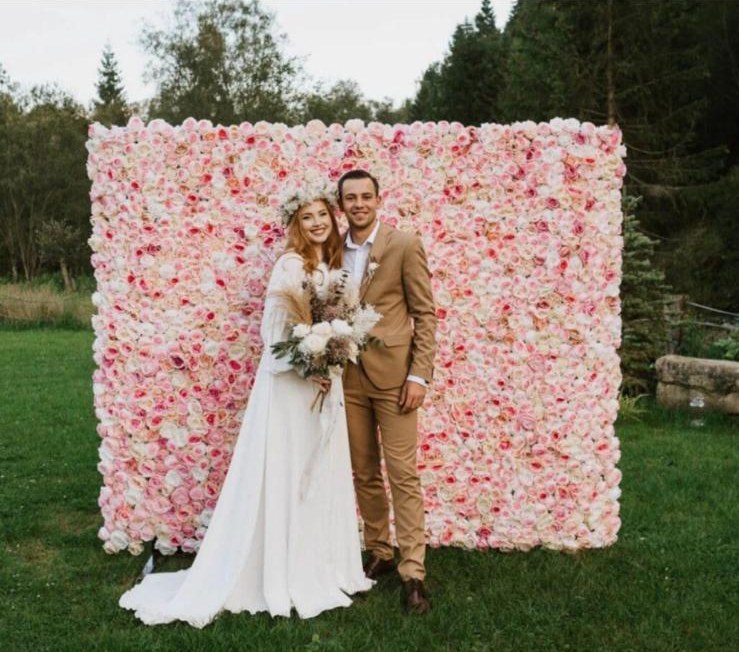 Couple posing in front of a flower wall wedding backdrop